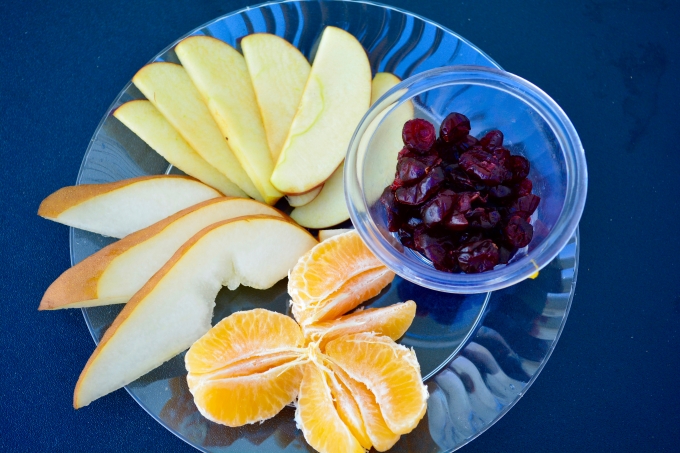 Sliced apple, pear, clementine wedges and small glass bowl of dried cranberries on a glass plate for renal diet snack options